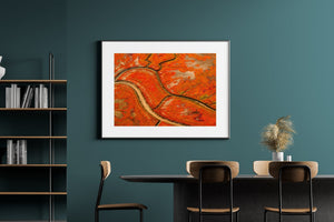 A broad pale channel curves through red-orange marshland seen from above.