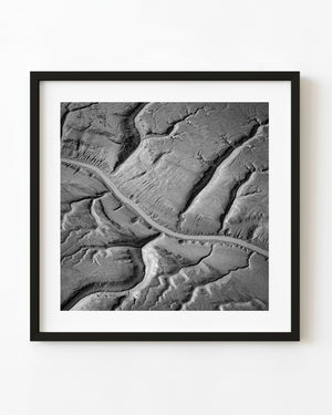 Pale curving tidal channel across textured Alaska coastal flats in black and white.