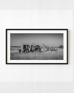Vintage tractor and seeder in tall Alberta prairie grass beneath an open sky, black and white.