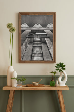 Converging stone walls frame an American flag and a tall gridded window in Manhattan’s Grand Central.