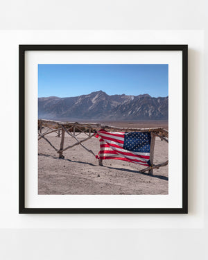 An American flag drapes over a rough fence before an open plain and mountain ridge at a Japanese American camp memorial.