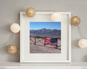 Deep gullies mark the distant mountain ridge beyond an American flag and rustic fence.