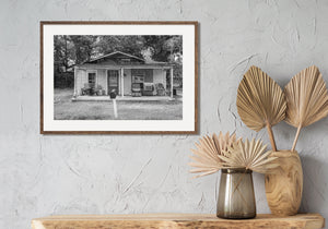 Pale porch posts and worn walls stand against darker trees around a rural house.