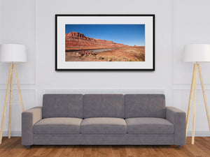 Red rock folds cast deep shadows above scattered stones and clumps of desert vegetation.