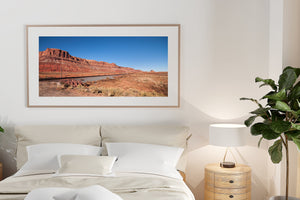 Warm desert cliffs contrast with a dark straight rail line and pale dry ground in the American Southwest.