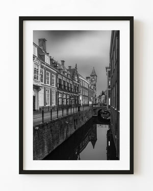 Brick waterfront buildings and a clock tower reflect in an Amersfoort canal in black and white.