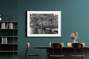 Fine ripples reflect light below brick houses, leafy trees and covered boats.