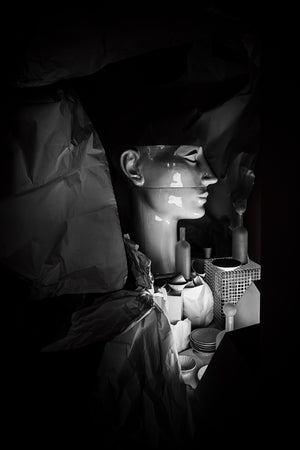 Glossy mannequin head amid crumpled paper and small objects in an Amsterdam shop display.