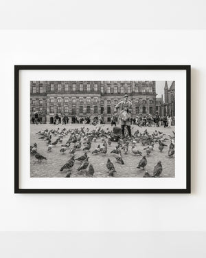 Pigeons and a man in Amsterdam Dam Square before the Royal Palace, photographed in black and white.