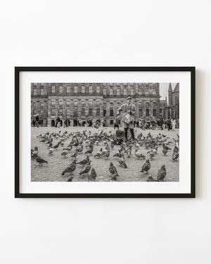 Pigeons and a man in Amsterdam Dam Square before the Royal Palace, photographed in black and white.