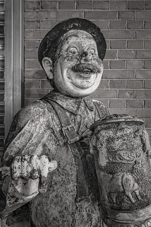 Grinning pub mascot with a moustache and large decorated beer stein against brick.