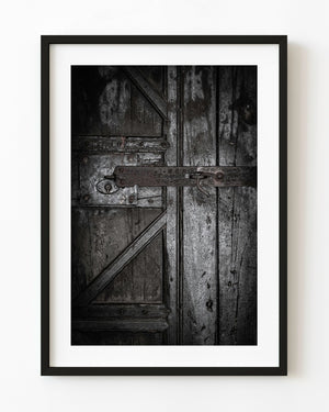 Weathered wooden door with a long iron latch and old lock photographed in monochrome.