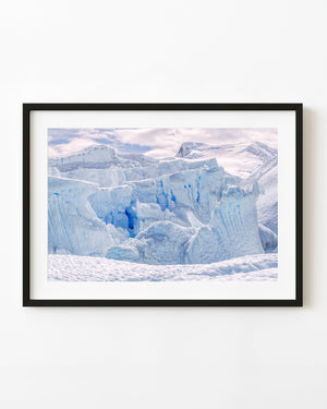 Blue Antarctic ice crevasses and fractured walls above rippled snow beneath a pale sky.