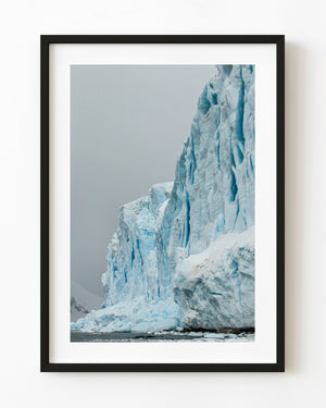 Tall Antarctic blue ice wall with deep cracks above a narrow strip of dark water.