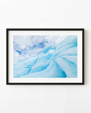 Blue Antarctic iceberg curves with a small opening beneath a streaked cloudy sky.
