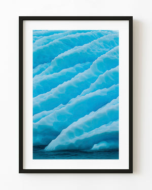 Turquoise Antarctic iceberg with diagonal white ridges and blue hollows above dark water.