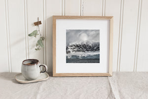 Fractured coastal cliffs with snow-covered ridges beneath a soft cloud formation.