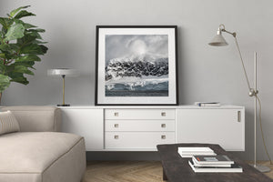Antarctic landscape with dark sea, snow-streaked rock and towering pale clouds.