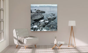 Antarctic coastal rocks lead toward a pale glacier across the water.