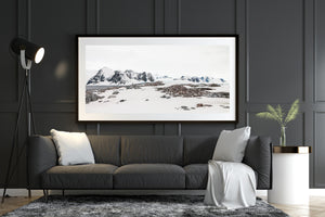 Snowfields and exposed rocks lead toward a gentoo penguin colony and distant mountains.