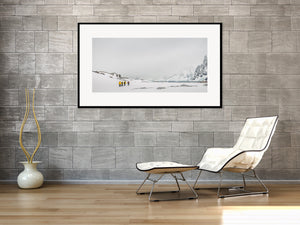 Misty Antarctic mountain cliffs rise above a snowy shore and a small group of walkers.
