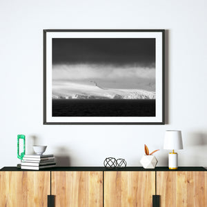 Dark storm clouds gather above Antarctic ice cliffs and calm ocean water.