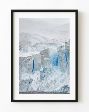 Deep blue crevasses divide pale Antarctic ice cliffs beneath a snowy slope.