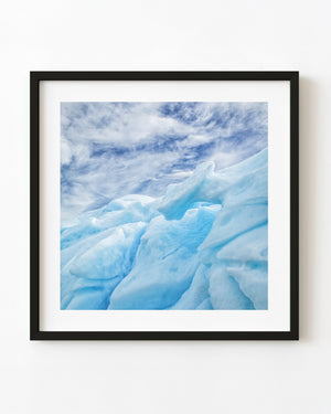 Blue ridges and sculpted recesses of an Antarctic iceberg viewed from below beneath wispy white clouds.