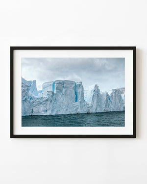 A long Antarctic iceberg with irregular cliffs and deep blue crevices above dark rippled water.