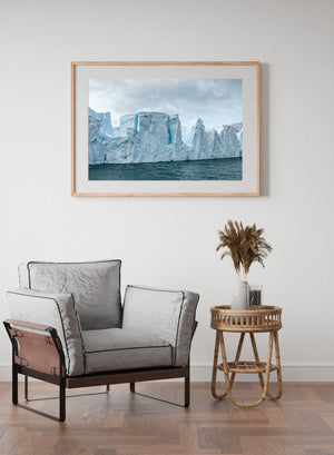 Colour Antarctic seascape with a long sculpted iceberg beneath subdued clouds.
