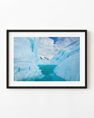 Turquoise water fills a narrow pool between pale blue Antarctic ice walls beneath clouds.