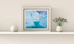 A narrow opening between iceberg walls reveals snow-covered mountains and blue sky.