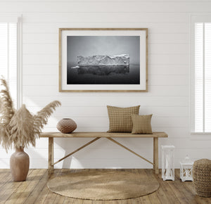 Black and white Antarctic seascape with a large iceberg and smaller floating ice nearby.