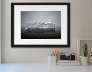 A broad iceberg and its reflection beneath falling snow in Antarctica.