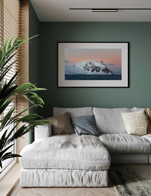 Snowy coastal peaks rise from deep blue water beneath a softly coloured evening sky.