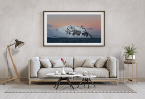 Antarctic mountain landscape with pink sky, blue-white snow and dark rippled sea.