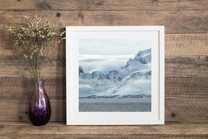 Pale blue shadows across snowy Antarctic mountains above grey water.