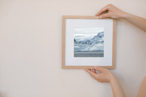 Grey water below a fractured ice shore and snow-covered Antarctic mountains.