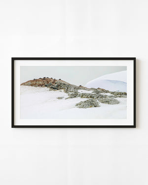 Penguins nesting along a rocky Antarctic ridge above snow.