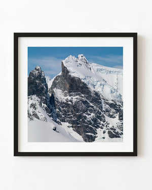 Antarctic rock peaks beneath bright snow ridges and blue sky.