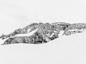 A broken band of Antarctic stone between white snow and pale sky.