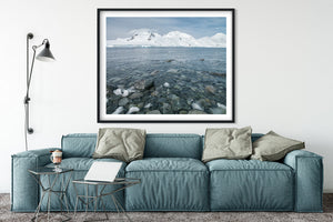 Small ice pieces among dark stones along an Antarctic shore.