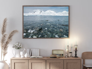Snow-covered Antarctic mountains across blue-grey coastal water.