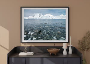 An Antarctic seascape with rocky shallows and distant snow ridges.