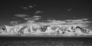 Snowy Antarctic coastline beneath streaks of cloud and a broad dark sky.