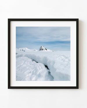 Antarctic snowfield with a dark foreground break and distant rock peak.