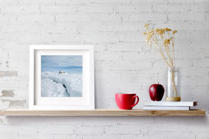 Square Antarctic landscape with pale blue sky, snow banks and a distant peak.