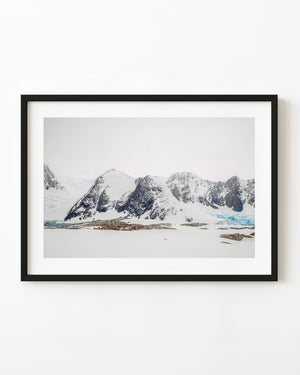 Snowy Antarctic mountains and a pale blue glacier above an open snowfield.