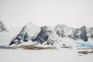 Dark Antarctic rock faces rising beyond white snow and blue ice.