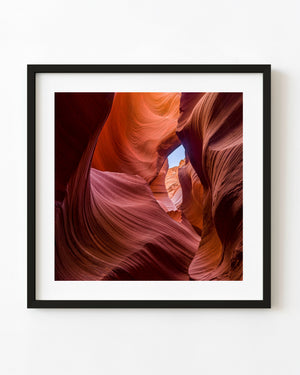Orange and red Antelope Canyon sandstone curves around a small blue sky opening.
